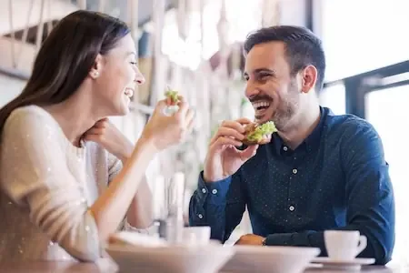 Two friends laughing and eating together at a cafe table