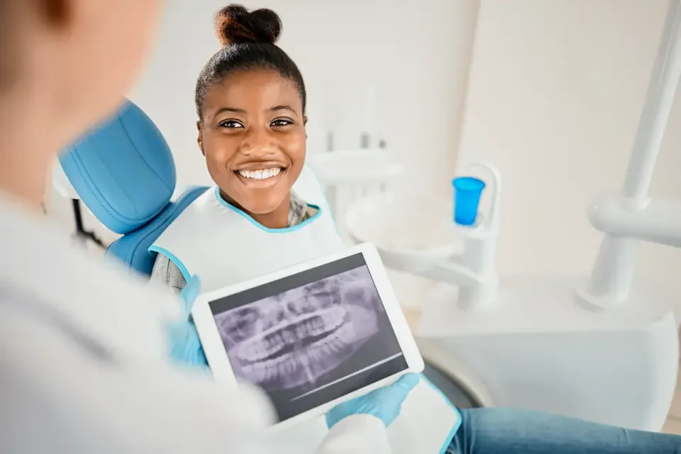 Smiling young patient in a dental chair holding a tablet that shows a panoramic X-ray